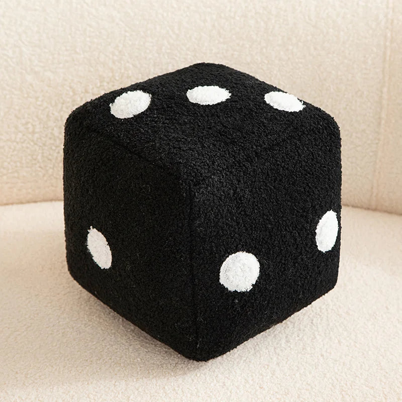A black plush dice cube with white polka dots resting on a light surface.