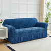A deep blue anti-slip jacquard sofa slipcover is displayed on a light rug in a bright room.