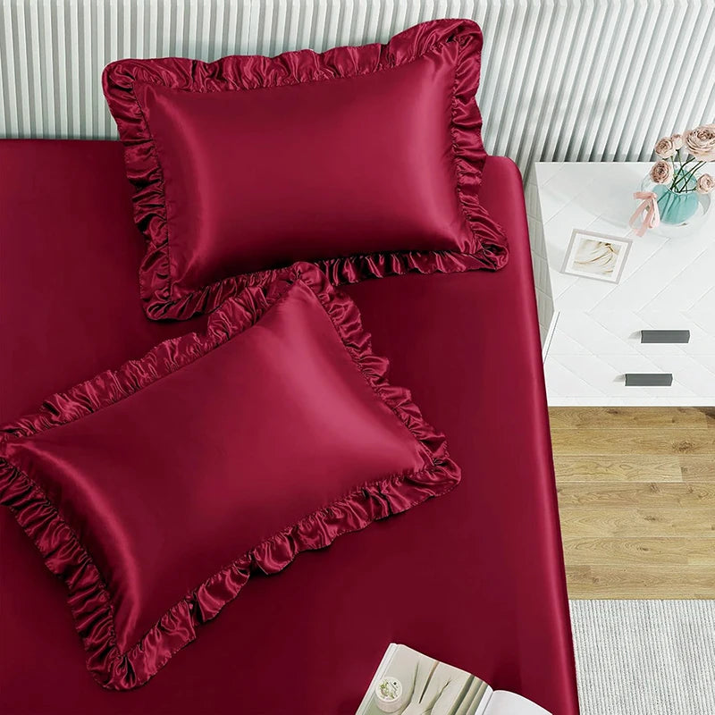 A set of two deep burgundy ruffled satin pillowcases displayed on a red surface.