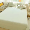 A light green and white gingham organic cotton bedding set featuring a flat sheet, pillowcases, and a small teddy bear.