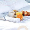 A set of white kitchen cleaning cloths with blue stripes resting on a white tray next to a cup of coffee and fresh orange sli