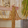 A hand is holding long, golden decorative door string curtains that drape down like a curtain.