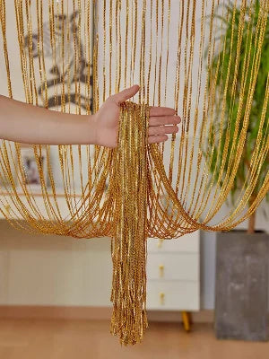 A hand is holding long, golden decorative door string curtains that drape down like a curtain.