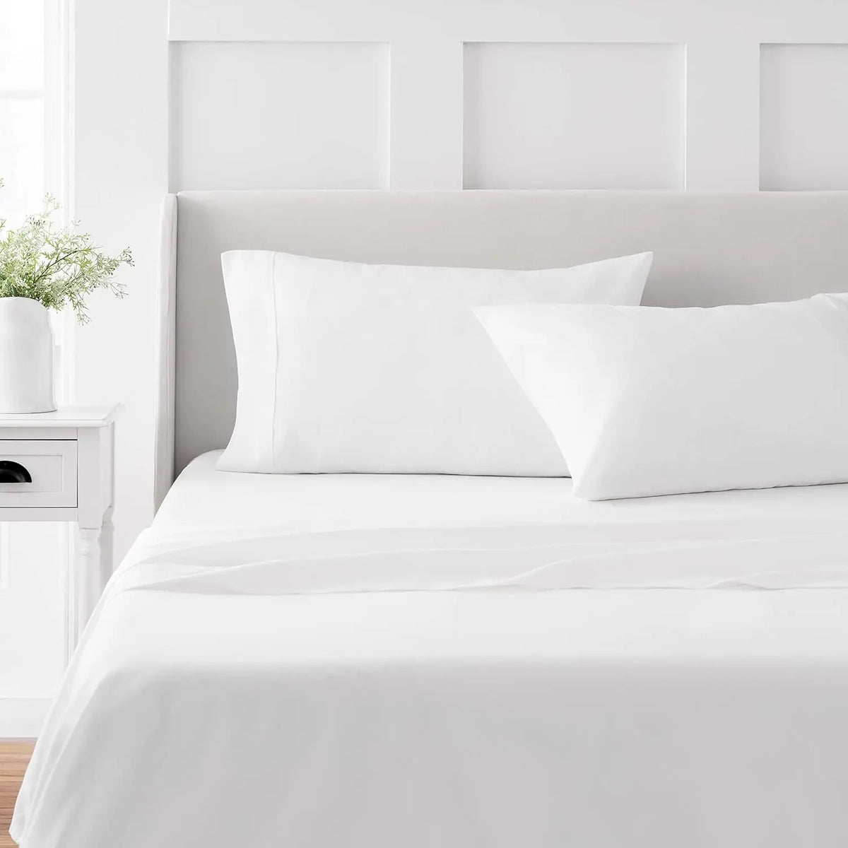 A white bed with a headboard and bedding, featuring a 4-piece microfiber flat fitted sheet set.