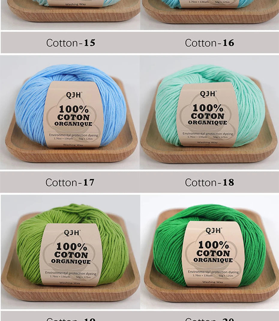 A set of ten skeins of 100% organic cotton yarn in various shades of blue and green, displayed on wooden trays.