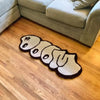 A cute cartoon decorative floor mat shaped like a body lying down on a wooden floor.