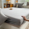 A fitted gray bed sheet is draped over a bed, with a hand resting on the fabric.