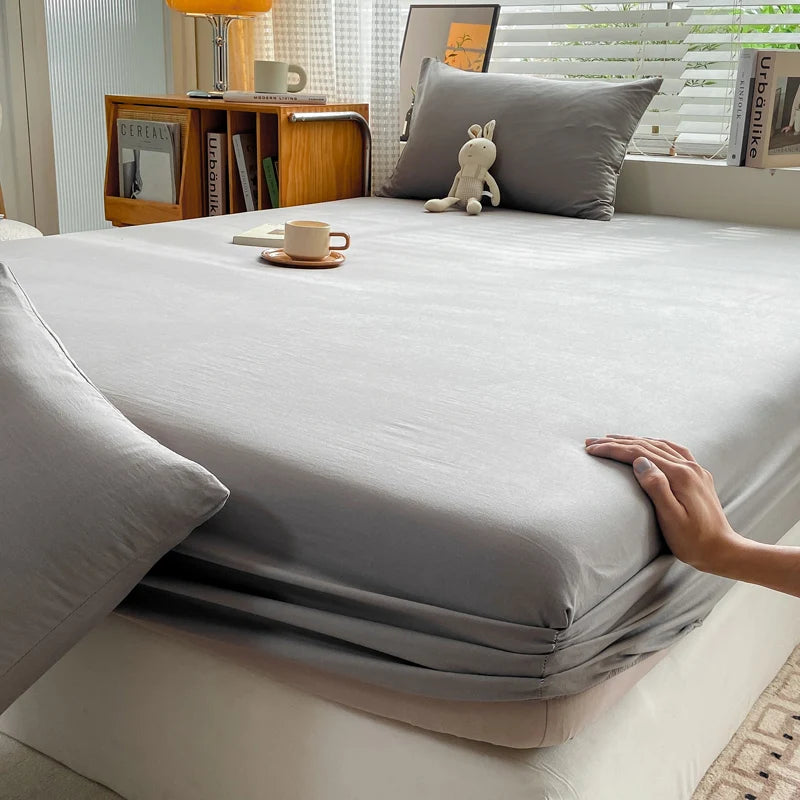 A fitted gray bed sheet is draped over a bed, with a hand resting on the fabric.