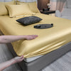 A luxurious gold fitted bed sheet is draped over a bed, with pillows and accessories visible.