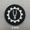 A black embroidered patch featuring a white gear design with a stylized animal head in the center.