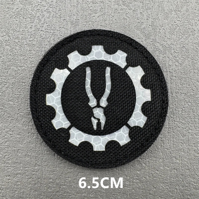 A black embroidered patch featuring a white gear design with a stylized animal head in the center.