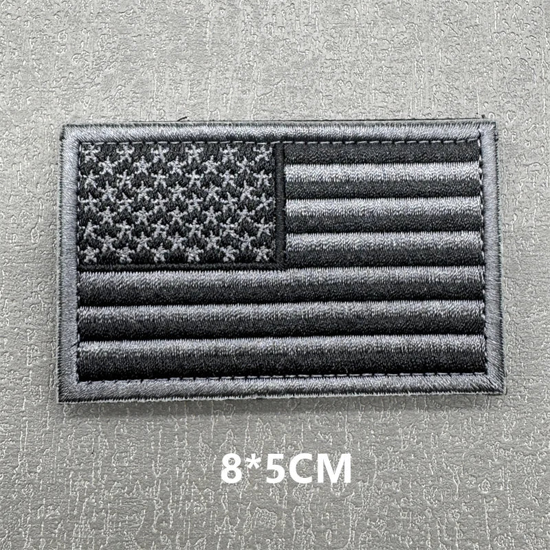A black and gray USA flag patch with horizontal stripes and stars, featuring hook and loop backing.