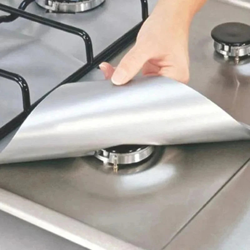 A hand places a silver reusable aluminum stove burner protector mat onto a stovetop grate.