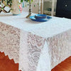 A white vintage lace tablecloth covers a rectangular dining table set with blue plates and floral arrangements.