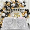 A silver sequin rectangle table cover draped on a table, surrounded by gold and black balloons and a 'Happy Birthday' sign.