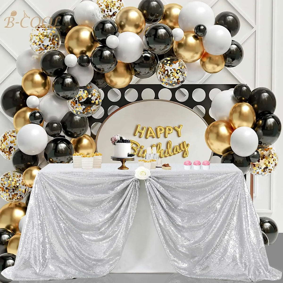A silver sequin rectangle table cover draped on a table, surrounded by gold and black balloons and a 'Happy Birthday' sign.