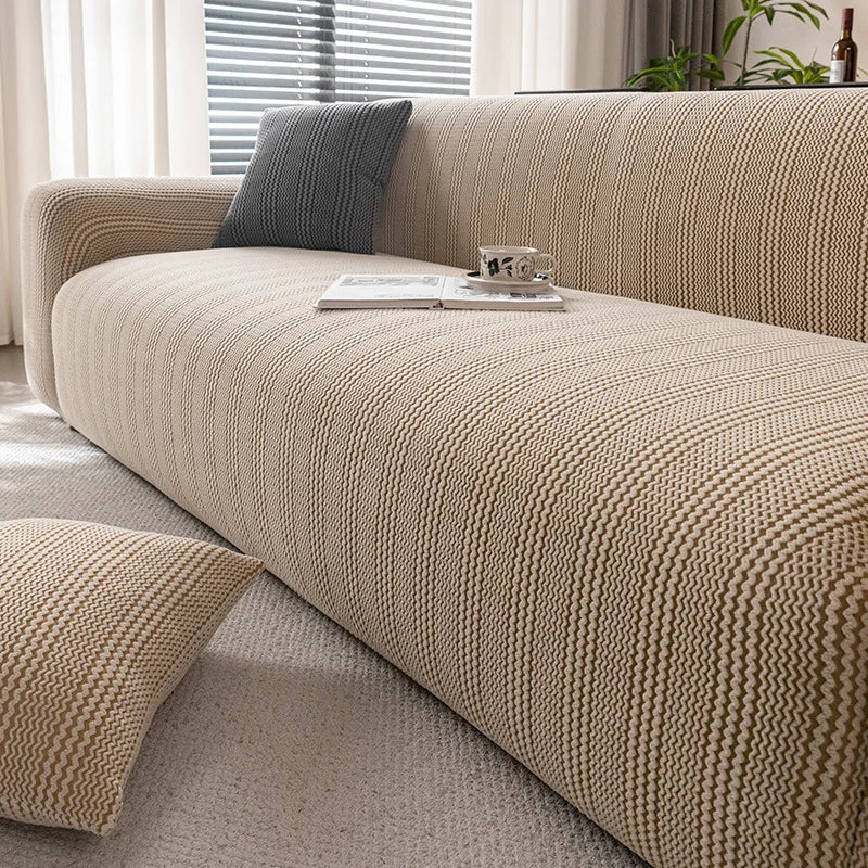 A beige textured sofa slipcover with a dark gray throw pillow and books on the cushion.
