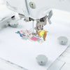 A close-up of a sewing machine embroidery hoop being used to stitch a colorful map design onto white fabric.
