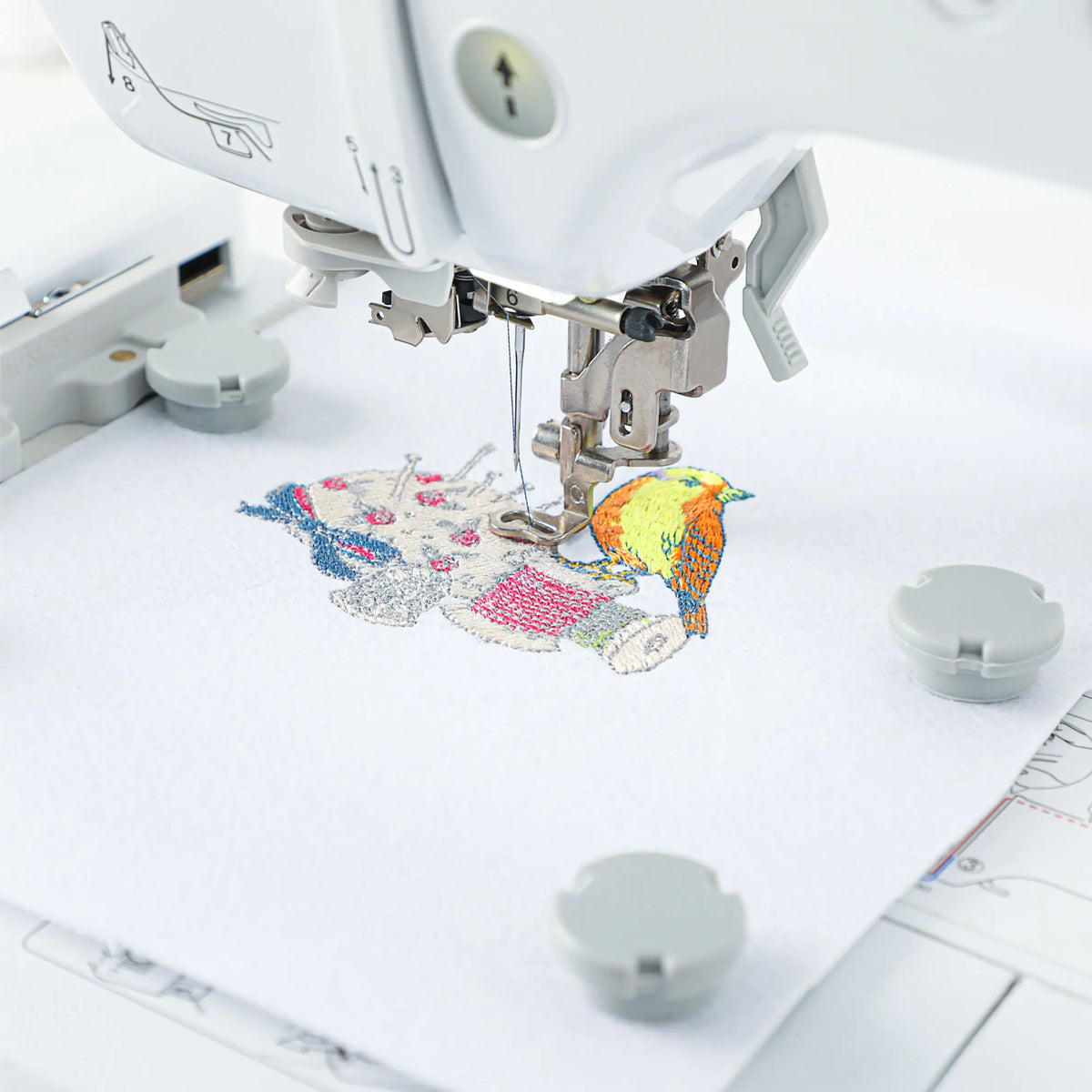A close-up of a sewing machine embroidery hoop being used to stitch a colorful map design onto white fabric.