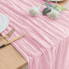 Pink pleated cheesecloth table runner with white roses and gold cutlery on a wooden table.