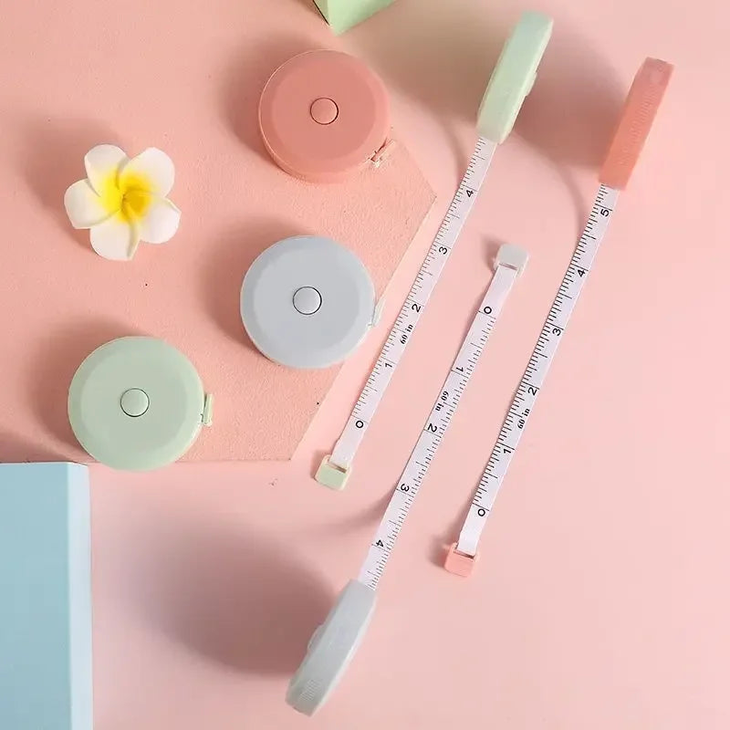 A collection of pink and mint green retractable double-sided measurement tapes arranged on a light pink background.