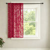 A sheer red lace curtain with a wave border hanging in a white window frame.