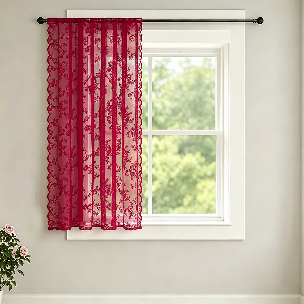 A sheer red lace curtain with a wave border hanging in a white window frame.