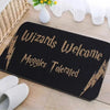 Black entrance mat with gold text reading Wizards Welcome Muggle Tolerated placed on a wooden surface.