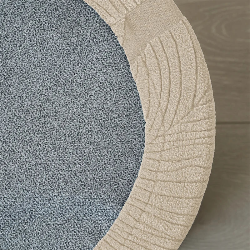 A round ottoman footrest slipcover featuring a textured gray fabric and a beige ribbed trim.