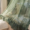 Sheer floral lace curtain panels in sage green and cream draped over a bed.