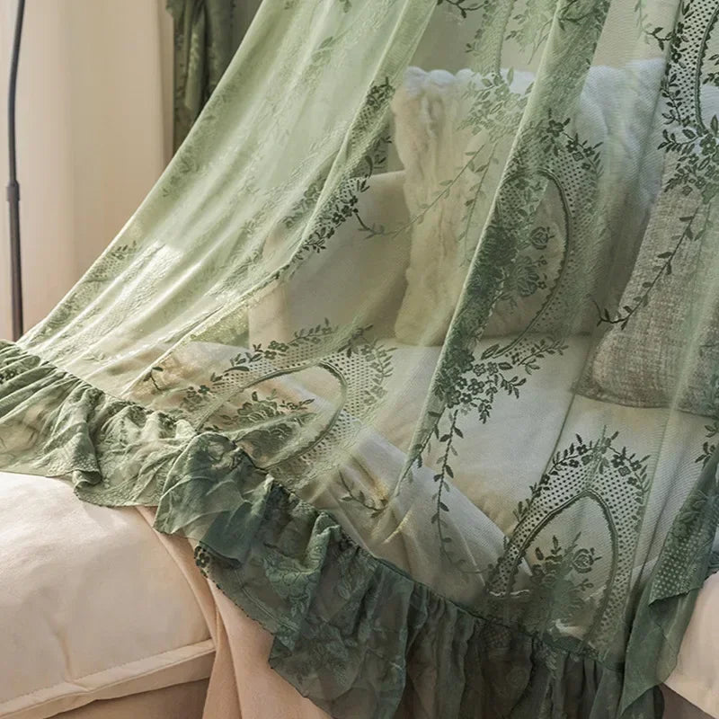 Sheer floral lace curtain panels in sage green and cream draped over a bed.