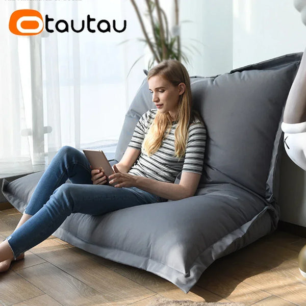 A woman relaxing on a gray outdoor bean bag cover indoors while looking at a tablet.