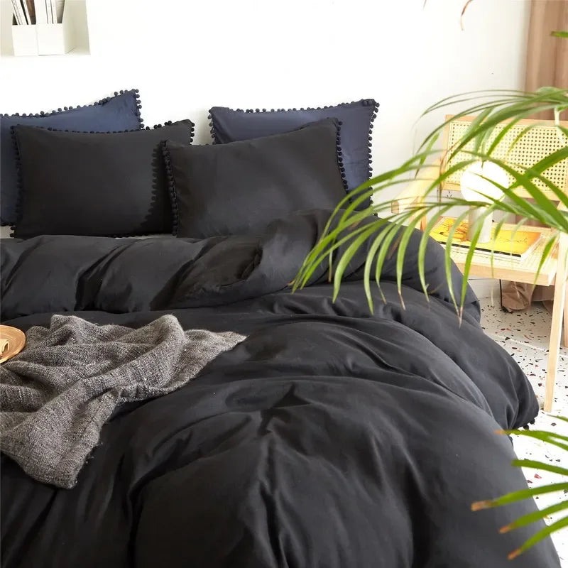 A black duvet cover set with dark blue pillows and a gray throw blanket on a bed.