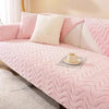 A pink plush sofa seat cushion cover with white accent pillows and a cup on the fabric.