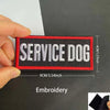 A hand holds a black and red embroidered patch with the text SERVICE DOG on it.
