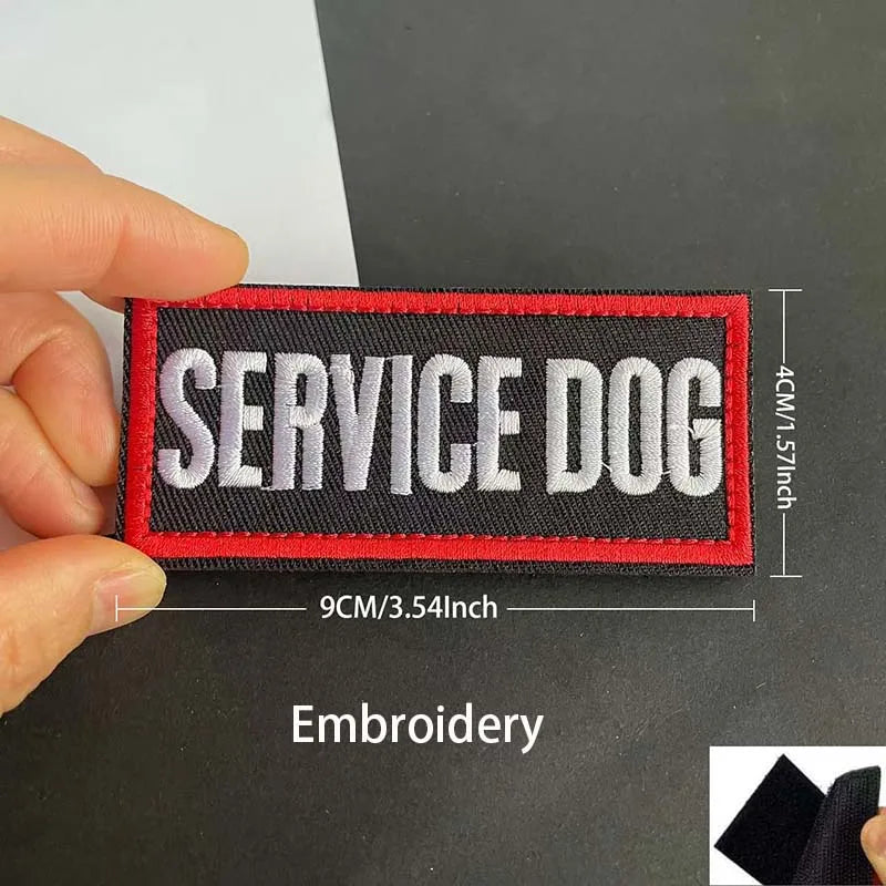 A hand holds a black and red embroidered patch with the text SERVICE DOG on it.