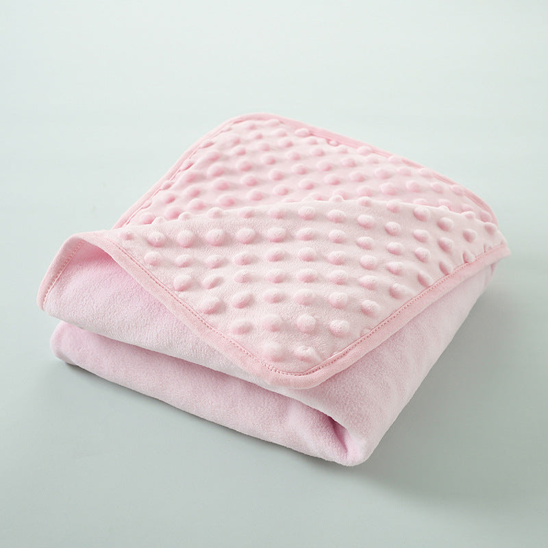 A pink, quilted fleece swaddle blanket folded neatly on a light gray surface.