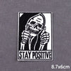 Black and white embroidered patch featuring a skull with hands to the face and the text STAY POSITIVE