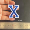 A hand holds a blue and white embroidered letter X patch, measuring 5x3.9 cm.