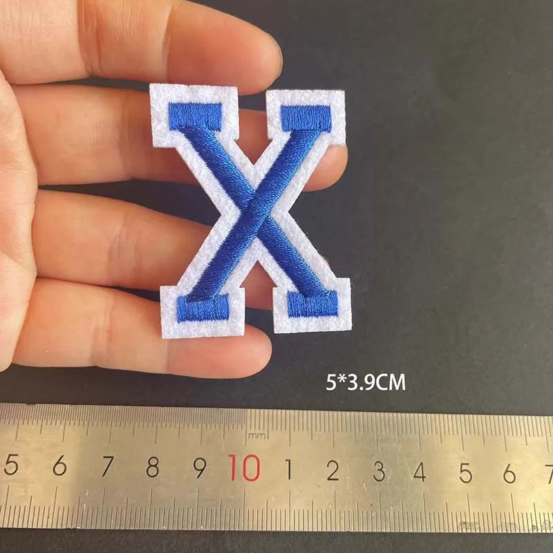 A hand holds a blue and white embroidered letter X patch, measuring 5x3.9 cm.