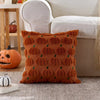 An orange knitted throw pillow cover with repeating pumpkin designs rests on a gray rug.