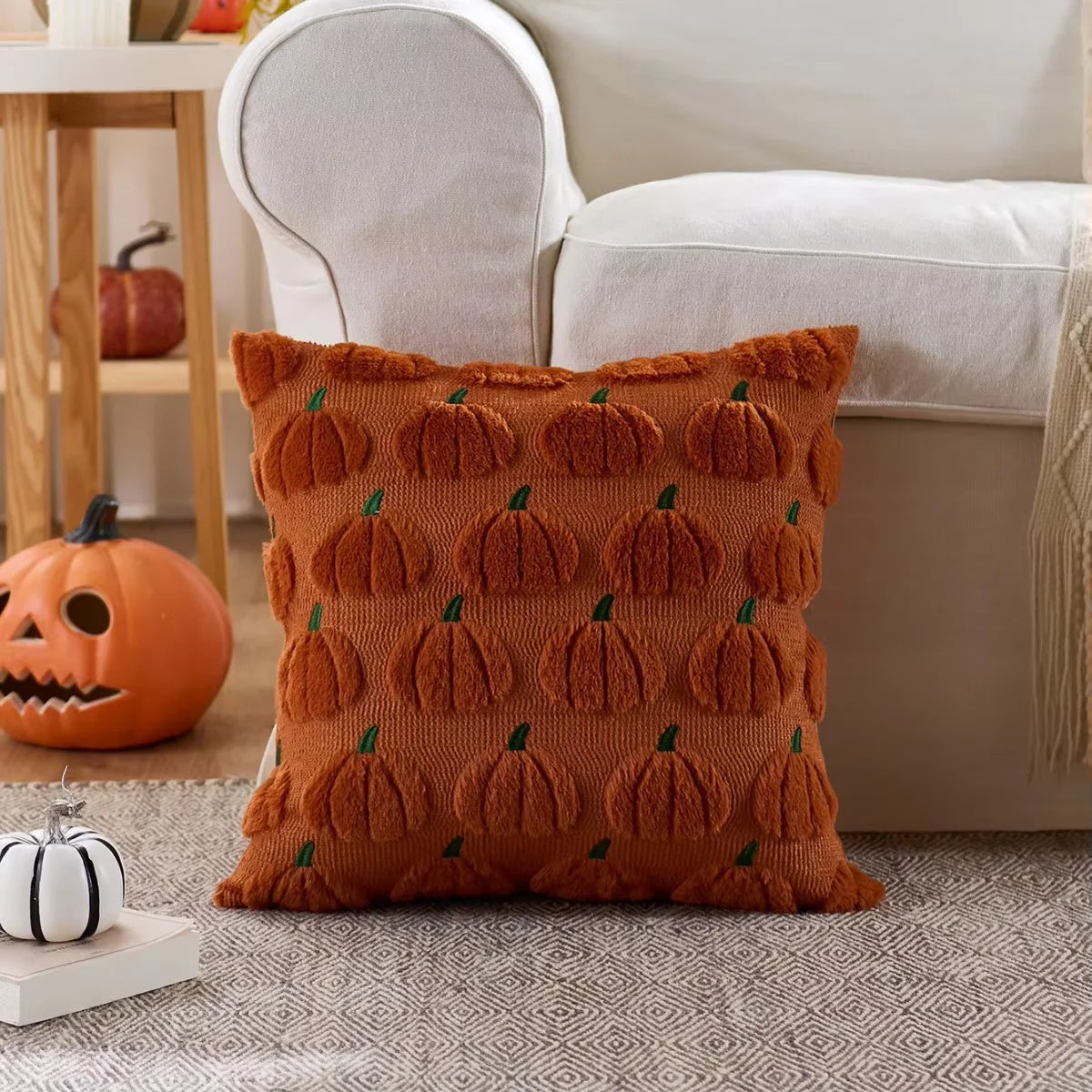 An orange knitted throw pillow cover with repeating pumpkin designs rests on a gray rug.