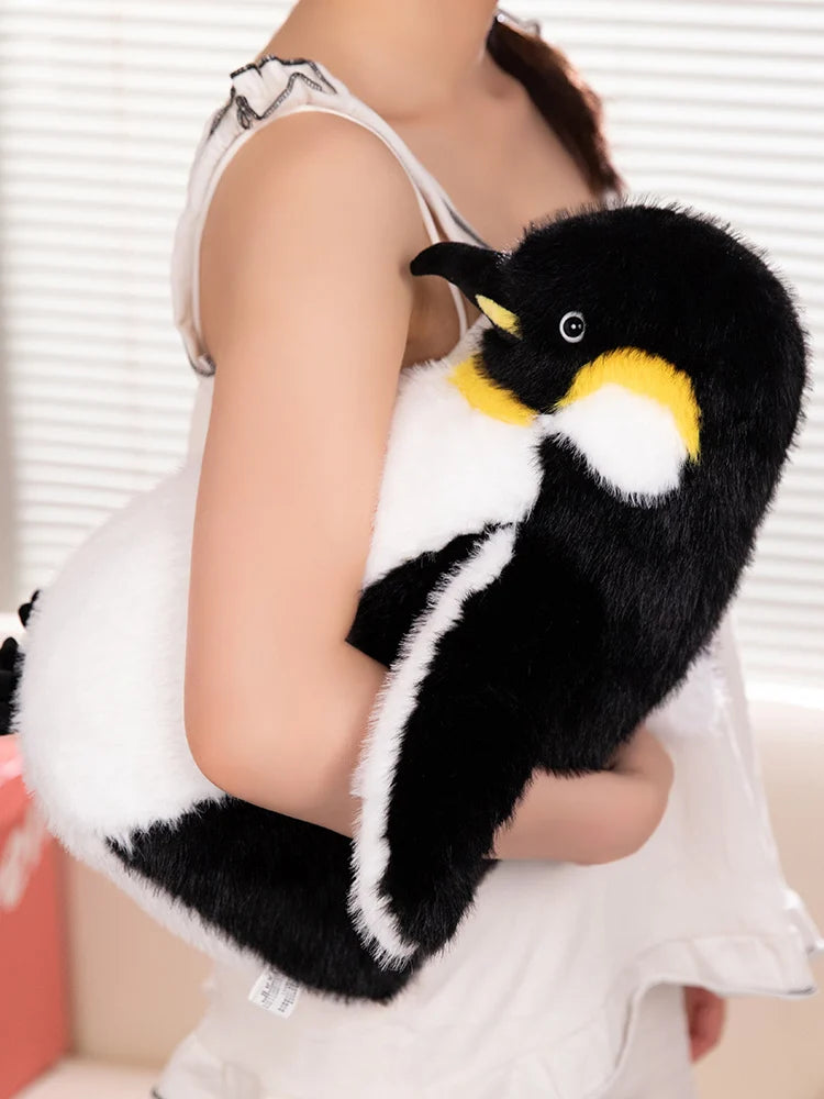A black and white plush toy of a penguin with yellow accents being held by a person.