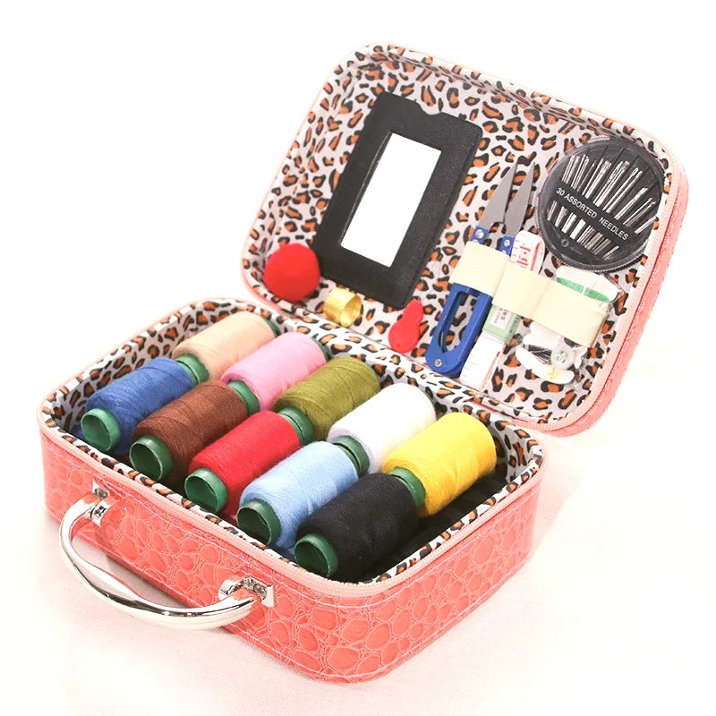 A portable sewing kit in a pink box featuring a mirror, scissors, needles, and various colored threads.
