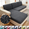 A gray stretch sofa seat cushion protector slipcover is shown on a light-colored sofa.