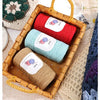 A wooden basket filled with three skeins of medium-thick hand-woven cotton yarn in red, light blue, and beige.