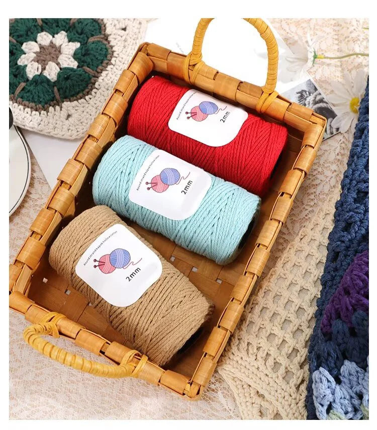 A wooden basket filled with three skeins of medium-thick hand-woven cotton yarn in red, light blue, and beige.