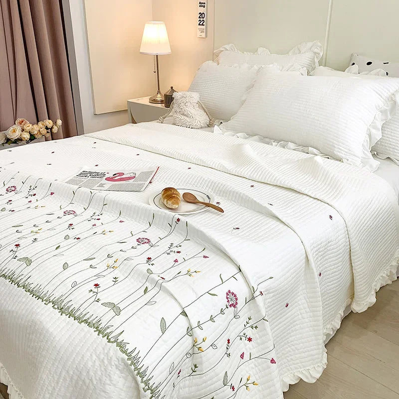 White quilted bedspread set with floral embroidery and a decorative pillow on a bed.