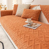 An orange knitted sofa cushion cover with cream accent pillows and a white cup on the fabric.