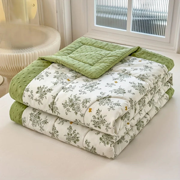 A stack of lightweight floral printed summer quilts in light green and white are displayed on a white surface.